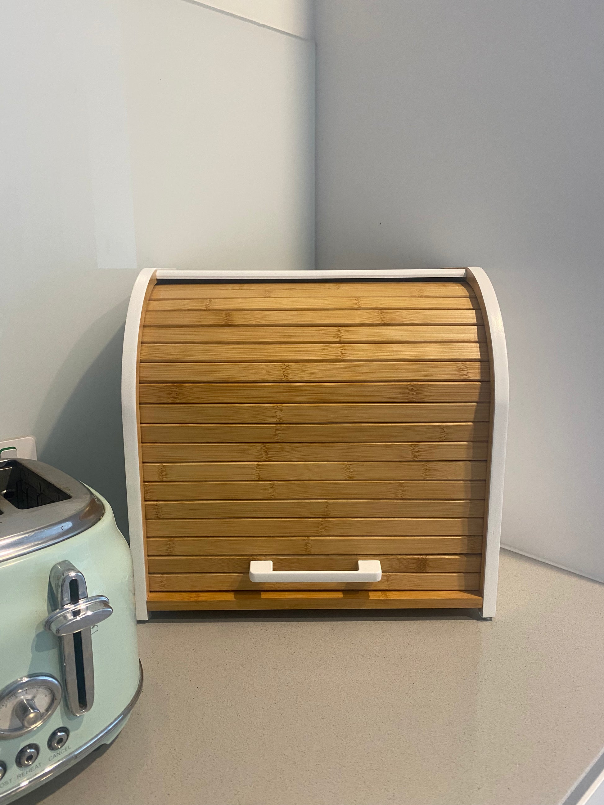 The Little Pantry Project bamboo bread box sitting on a kitchen bench next to a toaster.