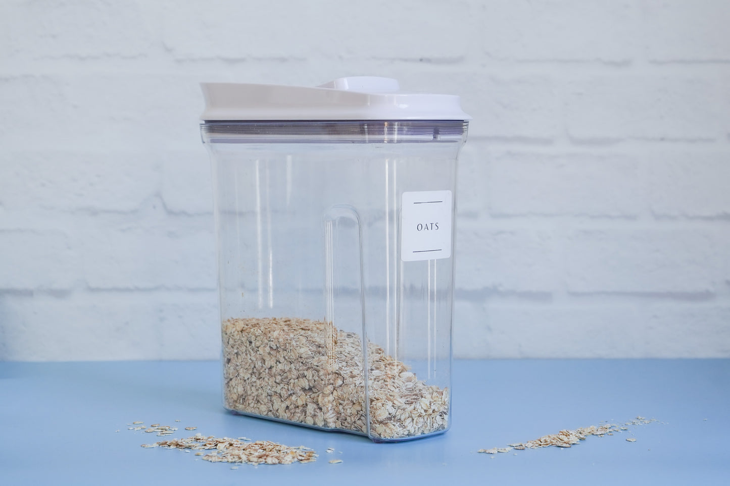 The OXO cereal container from The Little Pantry Project with oats inside and a label saying the words oats with two black lines under and above the word on a 45 degree angle.