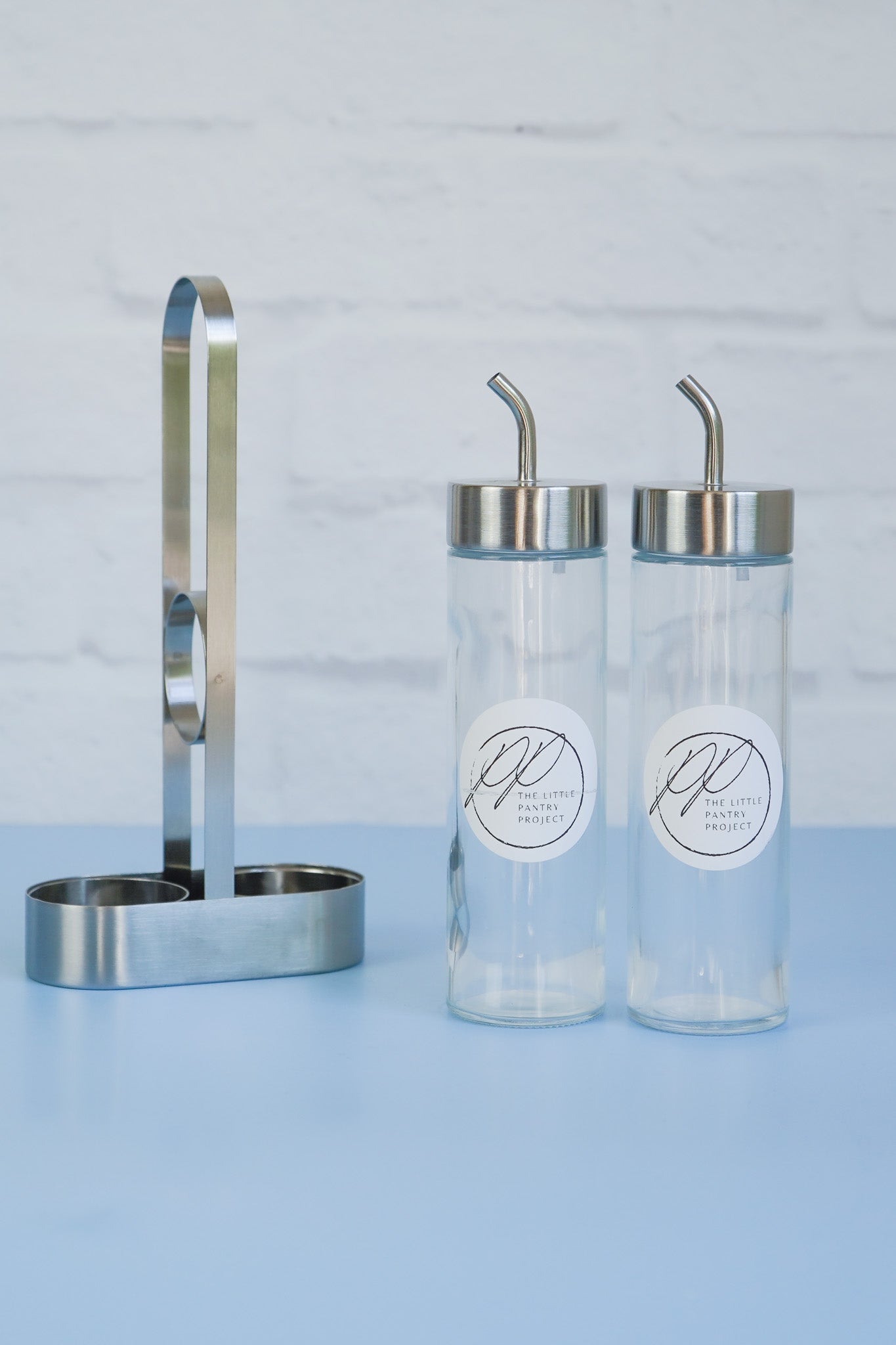 The stainless steel oil dispensers and carrier from The Little Pantry Project sitting separately next to each other.