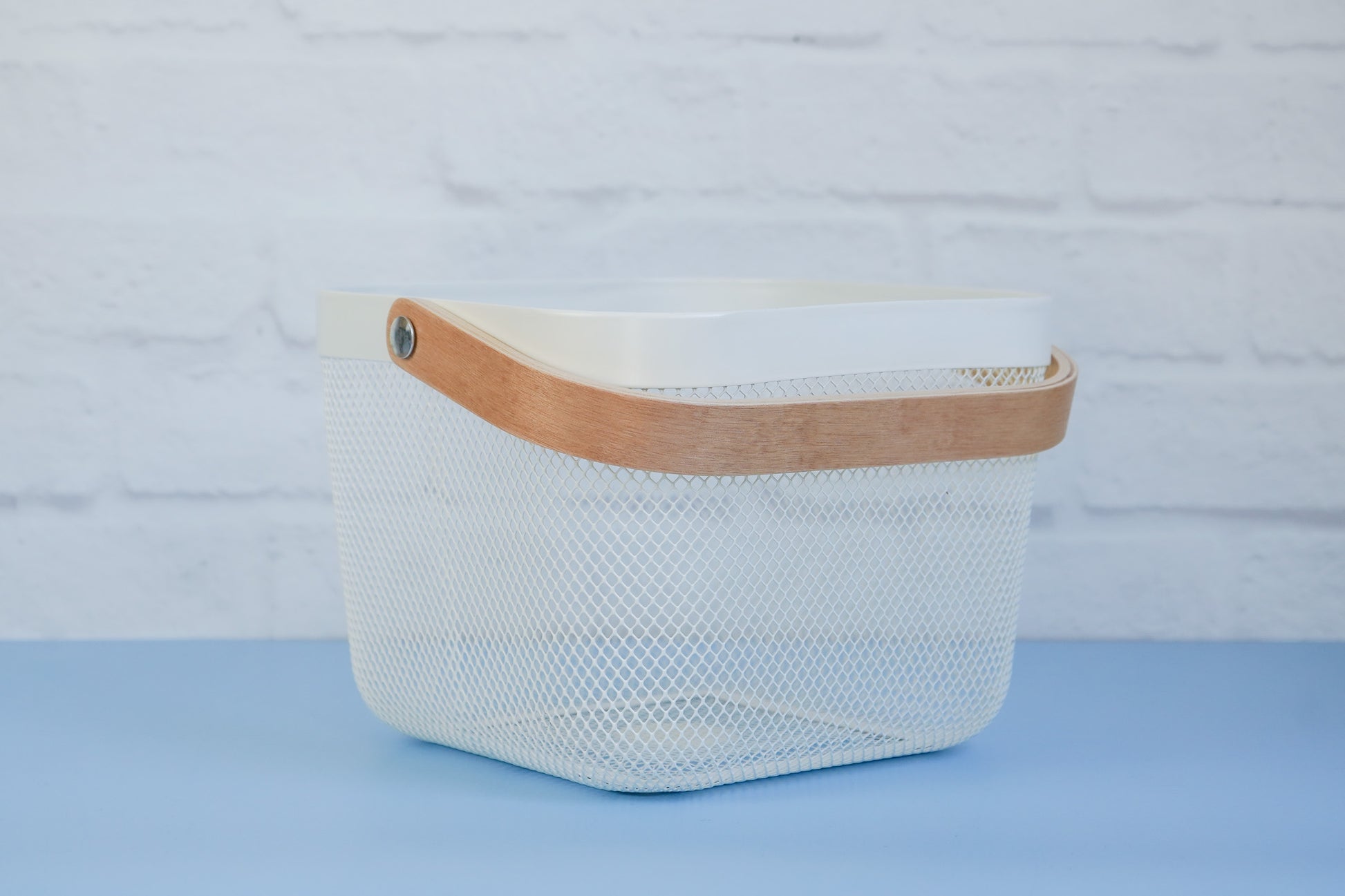 The white mesh basket with wooden handle from The Little Pantry Project on 45 degree angle.