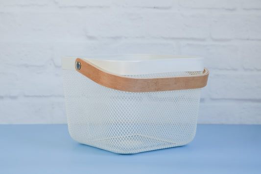 The white mesh basket with wooden handle from The Little Pantry Project on 45 degree angle.